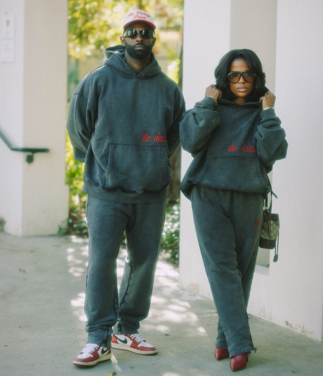 Two people wearing matching grey sweatshirt and pants sets with red text, standing outdoors.