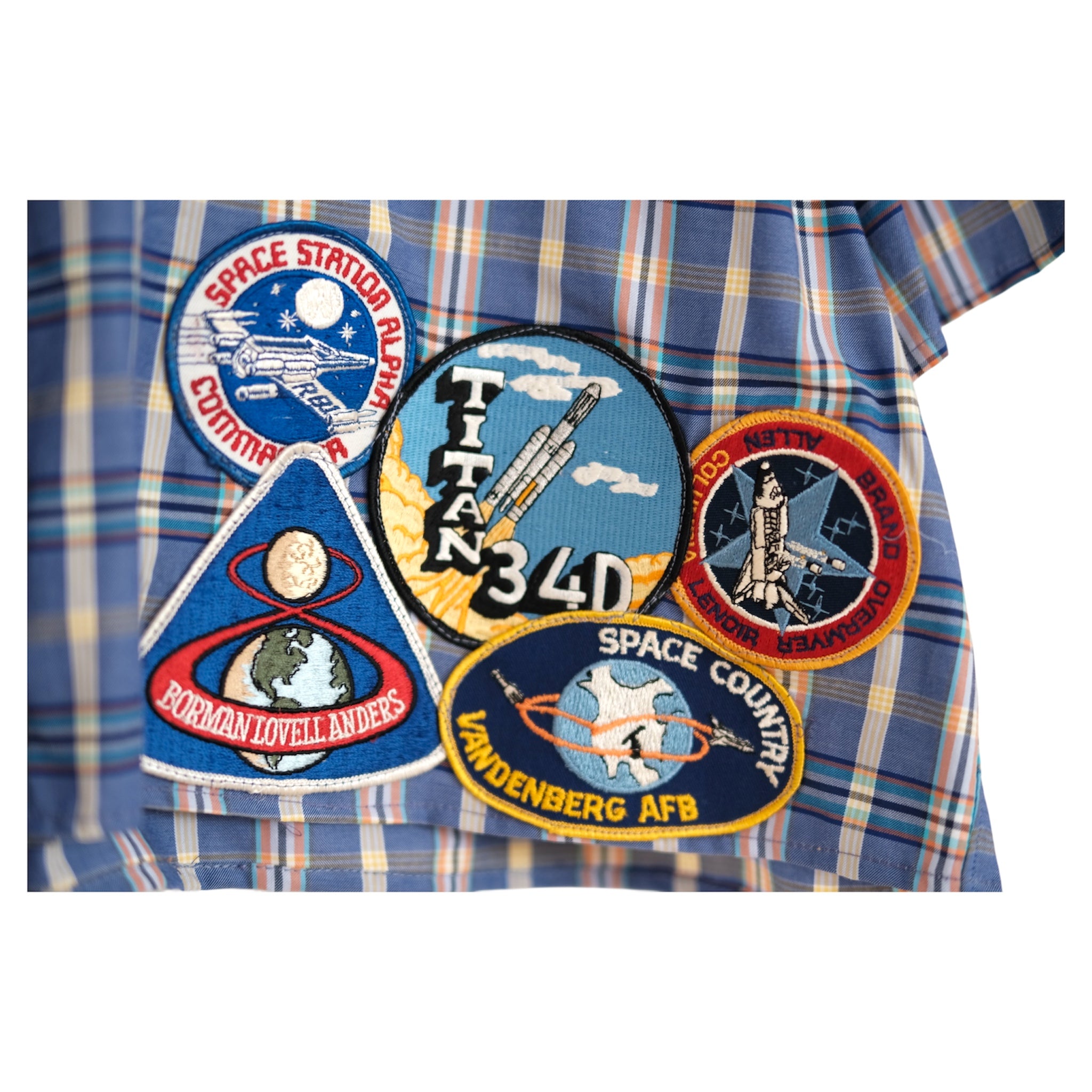 close-up of embroidered NASA mission patches sewn along the hem, including Challenger, Voyager and Titan 34D