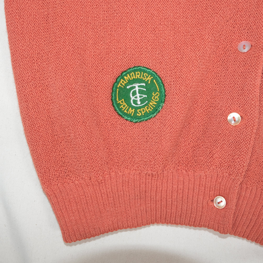 Close-up of a peach cardigan with a green logo on a white background