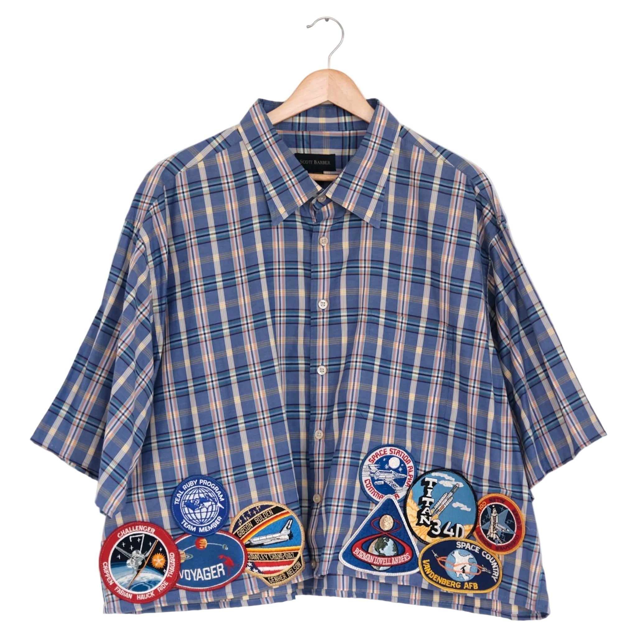 Blue plaid shirt with space-themed patches on a hanger against a white background