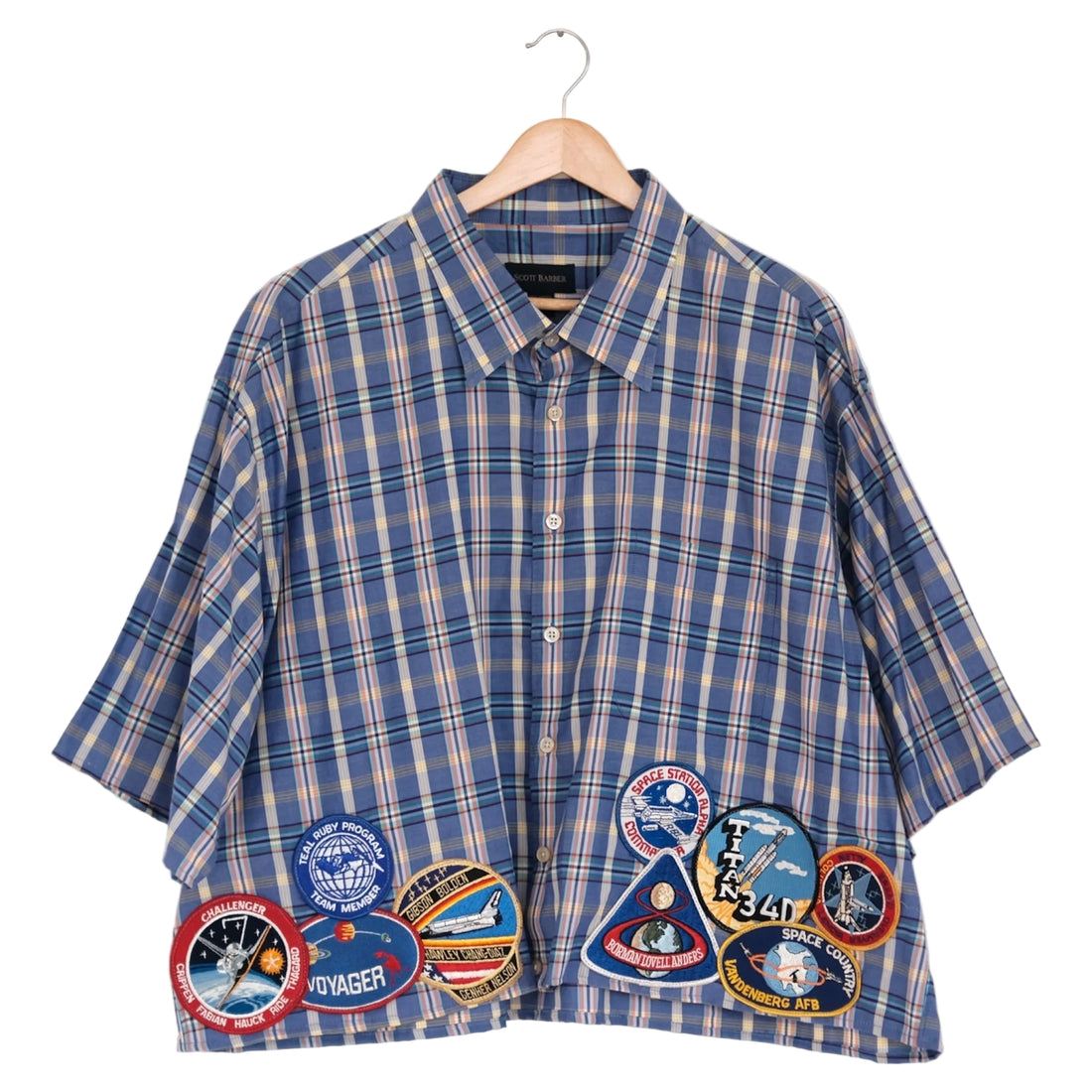 Blue plaid shirt with space-themed patches on a hanger against a white background